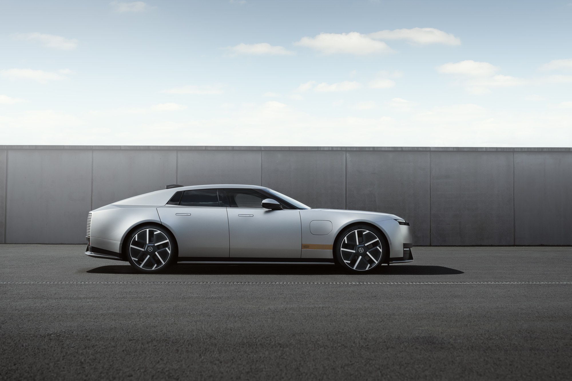 Silver Jaguar Type 01 electric four-door GT in side profile beside a concrete wall.