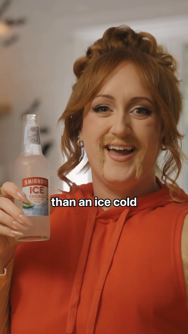 Brittany Broski wears a red hoodie and a drawn-on moustache while holding a clearly labelled Smirnoff Ice bottle.